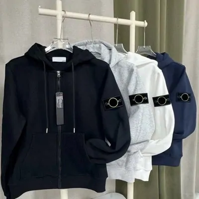 Dark hoodies and a shell jacket hanging in a row, one with a sleeve badge