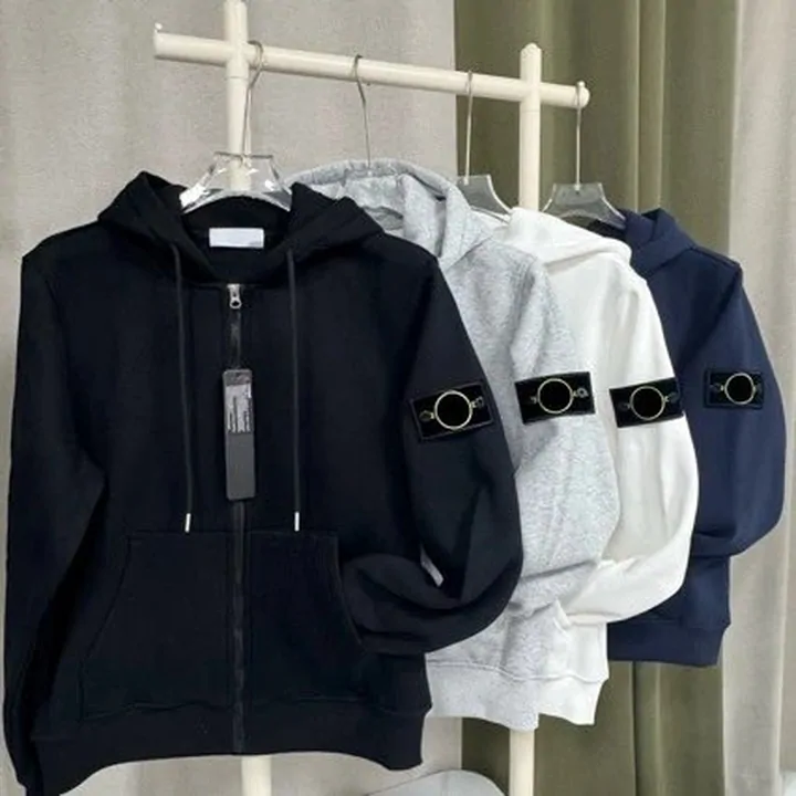 Dark hoodies and a shell jacket hanging in a row, one with a sleeve badge